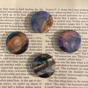 May include: Four colourful pinback buttons with space-themed images. The buttons feature a nebula, a galaxy, a space shuttle, and a quote about planes. The buttons are perfect for adding a touch of space to your belongings.