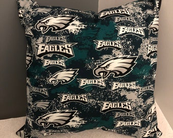 May include: A green and black cushion with a white Philadelphia Eagles logo repeated on the fabric. The logo is a stylised eagle with the word "Eagles" written below it.