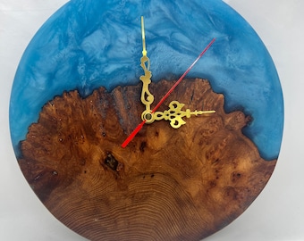 Puede incluir: Un reloj redondo de madera con una incrustación de resina azul. La esfera del reloj tiene agujas doradas y un borde dorado.
