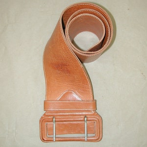May include: A brown leather belt with a large, rectangular buckle. The belt is rolled up and the buckle is visible in the center of the image.