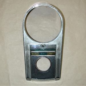 May include: Chrome motorcycle gauge housing with a round opening for a speedometer and a rectangular area with three small rectangular openings.