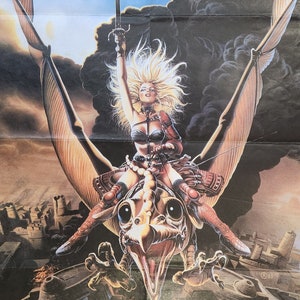 May include: A woman in a leather outfit rides a winged creature with a sword raised high. The creature has large eyes and a beak. The background is a dark sky with clouds and a cityscape.