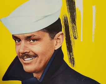 Può includere: Un uomo con un cappello da marinaio bianco e un cappotto blu scuro. Lo sfondo è di colore giallo brillante.