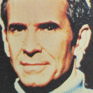 Może przedstawiać: Zbliżenie twarzy mężczyzny. Ma kr&oacute;tkie, ciemne włosy i nosi jasnoniebieską koszulę. Uśmiecha się.