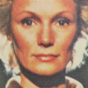 Może przedstawiać: Zbliżenie twarzy kobiety. Ma blond włosy, niebieskie oczy i nosi czarny kołnierzyk.