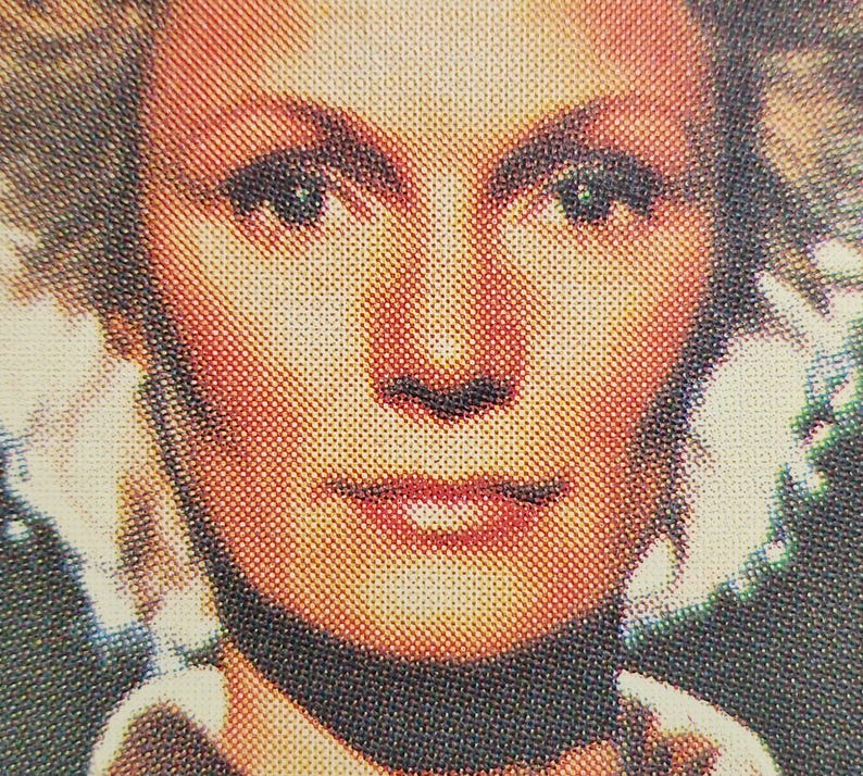 Może przedstawiać: Zbliżenie twarzy kobiety. Ma blond włosy, niebieskie oczy i nosi czarny kołnierzyk.