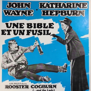 May include: A vintage movie poster for the film "Rooster Cogburn" starring John Wayne and Katharine Hepburn. The poster features a blue background with the title in white text and the actors' names in black text. The poster also includes a scene from the film with John Wayne and Katharine Hepburn.