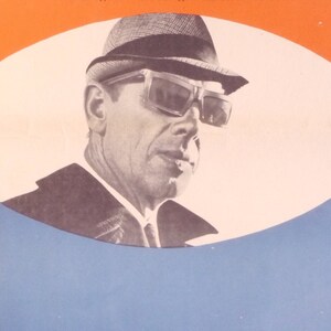 May include: A black and white photo of a man wearing a hat and sunglasses. The man is looking to the right. The photo is set against a background of orange, white, and blue.