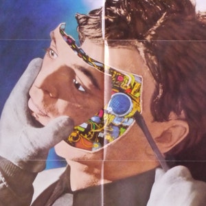 May include: An artistic illustration depicts a person's face with a section of the skin peeled back to reveal intricate circuitry and mechanical components. A gloved hand holds a tool near the face, suggesting a process of modification or repair. The background is a gradient of blue.