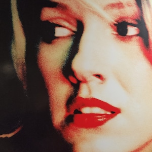 Puede incluir: Primer plano de la cara de una mujer con lápiz labial rojo y un toque de rubor rosado. Sus ojos están cerrados y su expresión es serena.