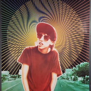 May include: A movie poster for the film "Slacker" featuring a young man wearing a red shirt and a baseball cap. The poster has a psychedelic background with yellow, green, and red lines radiating outwards. The text on the poster reads "Spellbinding... A scrappy and shrewdly hilarious first film" and "Exhilarating. There is nothing more amusing, original or outrageous on the current movie scene."