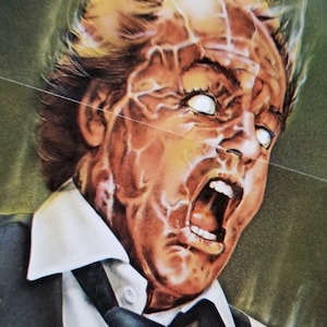 May include: A close-up of a man's face with a shocked expression. His skin is textured and his eyes are wide open. He is wearing a white shirt and a black tie.