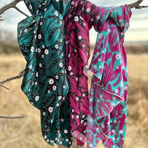 May include: Three colorful bandanas with a cactus and flower pattern. The bandanas are teal, pink, and black with white flowers and cacti.