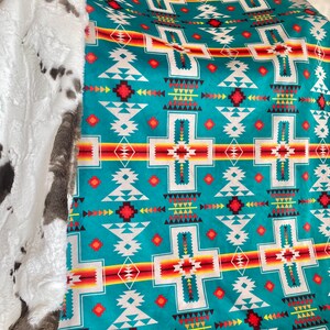 May include: A teal, red, white, and yellow patterned blanket with a white faux fur trim. The blanket features a geometric design with a Southwestern style.