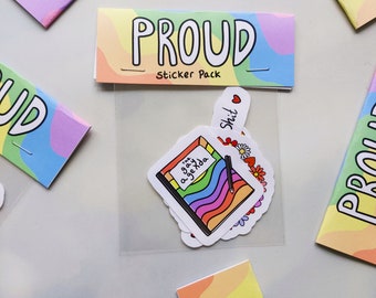 May include: A set of rainbow-themed stickers in a clear plastic bag. The stickers feature a rainbow heart, a rainbow notebook with the text "The Gay Agenda", and a hand holding a rainbow heart. The bag has a label that says "PROUD Sticker Pack".