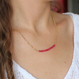 Puede incluir: Un collar de cadena dorada con una fila de pequeñas cuentas de color rosa brillante.