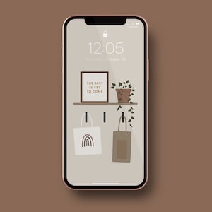 Può includere: Lo schermo di un telefono che mostra un orologio digitale con l'ora 12:05, la data giovedì 21 ottobre e una citazione motivazionale che dice "Il meglio deve ancora venire". La citazione è visualizzata in una cornice marrone con una pianta in vaso appesa a uno scaffale sopra. Due borse a tracolla sono appese sotto lo scaffale, una con un design arcobaleno e l'altra con una tasca marrone.