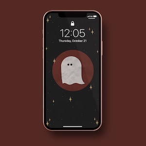 Puede incluir: Un teléfono inteligente con una pantalla negra que muestra una ilustración de un fantasma en un círculo rojo con estrellas doradas. La hora es 12:05 y la fecha es jueves 21 de octubre.