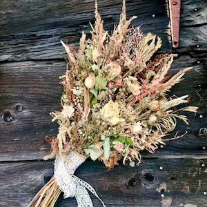 May include: A dried flower bouquet with a variety of dried grasses, flowers, and greenery. The bouquet is tied with a white lace ribbon and has a rustic, natural look.