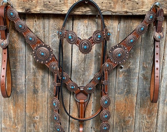 May include: A brown leather horse tack set with turquoise accents. The set includes a bridle, breast collar, and reins. The tack is decorated with intricate floral designs and metal conchos.