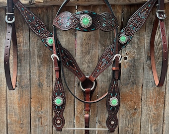 May include: A brown leather horse tack set with turquoise accents. The set includes a headstall, breast collar, and reins. The leather is decorated with floral patterns and silver studs.