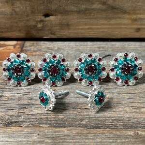 May include: Five silver-toned, round, decorative tacks with teal and red rhinestones. Two tacks have screws attached.