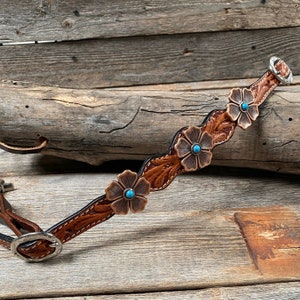 May include: A brown leather halter with a decorative floral design and turquoise accents. The halter has a silver buckle and is made of high-quality leather.