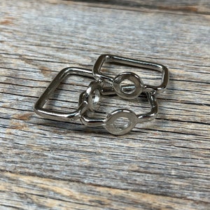 May include: Two silver metal D-rings, one slightly larger than the other, are stacked on top of each other. The rings are smooth and have a shiny finish.
