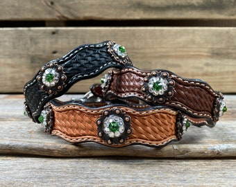 May include: Three leather collars with woven patterns and decorative metal accents. Each collar features a large, round, green gemstone surrounded by smaller clear rhinestones.