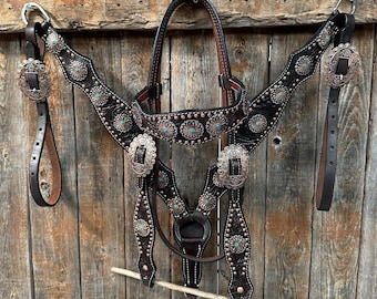 May include: A brown leather horse headstall with turquoise and silver accents. The headstall is decorated with floral designs and has a matching breast collar and reins.