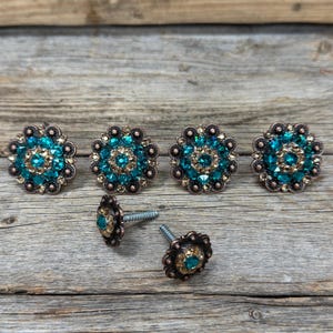 May include: Five turquoise and gold rhinestone concho buttons with a decorative design. The buttons are on a wooden surface.