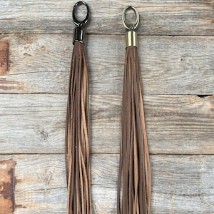 May include: Two brown leather tassels with metal rings and caps. One tassel has a silver cap and the other has a gold cap.