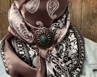 May include: A brown and white paisley patterned silk scarf with a decorative metal bolo tie. The bolo tie has a turquoise stone in the centre.