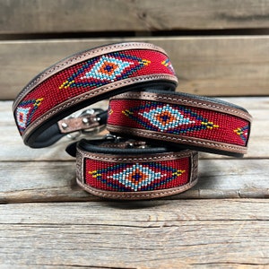 May include: Three leather dog collars with red, white, blue and green beaded designs. The collars are stacked on top of each other.
