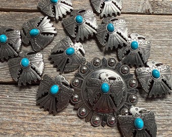 May include: A collection of silver-toned metal conchos featuring engraved geometric patterns and central oval turquoise cabochons. The set includes ten smaller bird-shaped conchos and one large circular concho with a central bird motif.