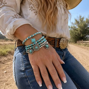 May include: A multi-strand bracelet set featuring turquoise-colored beads and silver-toned metallic beads. The bracelet includes several dangling charms, including a square turquoise stone, a round filigree medallion, and a small oval turquoise charm.