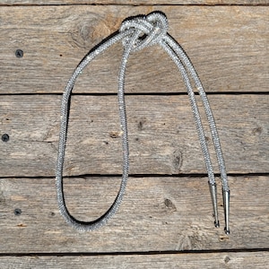 May include: A silver bolo tie with a rhinestone design. The tie is tied in a knot and the ends are finished with silver tips.