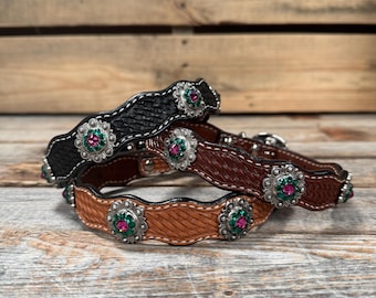 May include: Three leather dog collars with a wavy design and jeweled accents. The collars are black, brown, and tan. Each collar has a silver buckle and a row of silver flower-shaped embellishments with pink and green rhinestones.