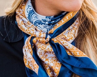 May include: A blue and gold paisley patterned bandana with a white background. The bandana is tied around a person's neck.