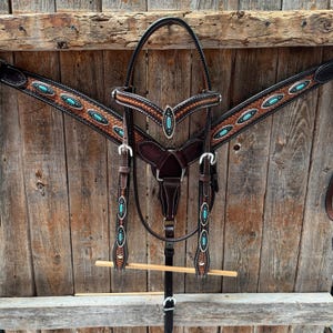 May include: A dark brown leather horse bridle and breast collar set featuring intricate basket weave tooling, white stitching, and silver-toned hardware. The set is decorated with oval-shaped turquoise stone inlays set in silver metal bezels.