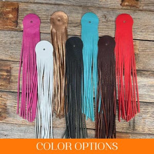 May include: A selection of leather fringe tassels in shades of pink, white, copper, black, turquoise, brown, and red. Each tassel features a circular top with a hole for hanging. The text "COLOR OPTIONS" is displayed in an orange rectangle.