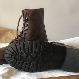 May include: Brown leather lace-up boots with a thick black rubber sole. The sole has a tread pattern with small flower-like designs.