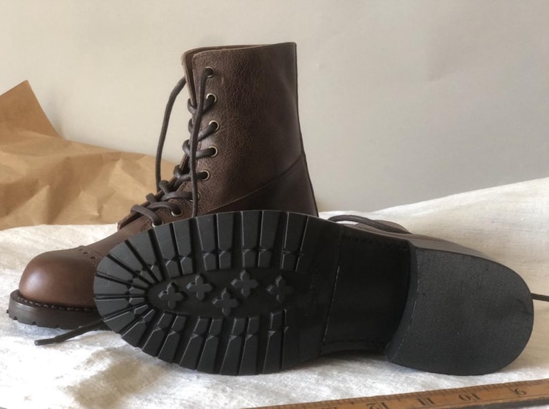 May include: Brown leather lace-up boots with a thick black rubber sole. The sole has a tread pattern with small flower-like designs.