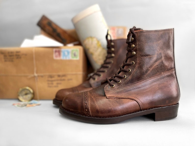 May include: A pair of brown leather lace-up boots with a cap toe design. The boots have a distressed look and are made of high-quality leather.