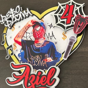Puede incluir: Un topper de pastel de cumplea&ntilde;os rojo y negro con un personaje de Spiderman, un micr&oacute;fono, una telara&ntilde;a y el nombre "Aziel" en letras rojas y negras. El topper de pastel tambi&eacute;n incluye el texto "Peso Pluma" en letras doradas.
