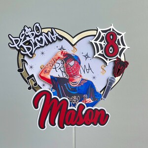 Puede incluir: Un adorno para pastel rojo y negro con una base en forma de coraz&oacute;n, un personaje de Spiderman, un micr&oacute;fono, una telara&ntilde;a y el texto "PESO BRUMA Mason" y "8".