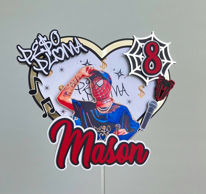 Puede incluir: Un adorno para pastel rojo y negro con una base en forma de coraz&oacute;n, un personaje de Spiderman, un micr&oacute;fono, una telara&ntilde;a y el texto "PESO BRUMA Mason" y "8".