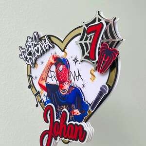 Puede incluir: Un topper de pastel de Spiderman rojo y negro con un fondo en forma de coraz&oacute;n. El topper presenta un personaje de Spiderman, un micr&oacute;fono, el n&uacute;mero 7 y el nombre "Johan".
