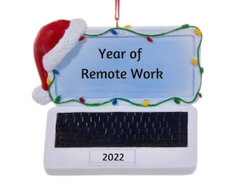 May include: White laptop Christmas ornament with a red Santa hat on the top. The screen says "Year of Remote Work" with colorful lights around the edge. The year 2022 is printed on the bottom.