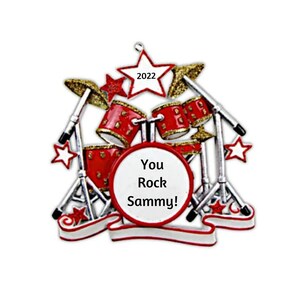 May include: Red and gold drum set Christmas ornament with a white star and the text "You Rock Sammy!" on a white banner.